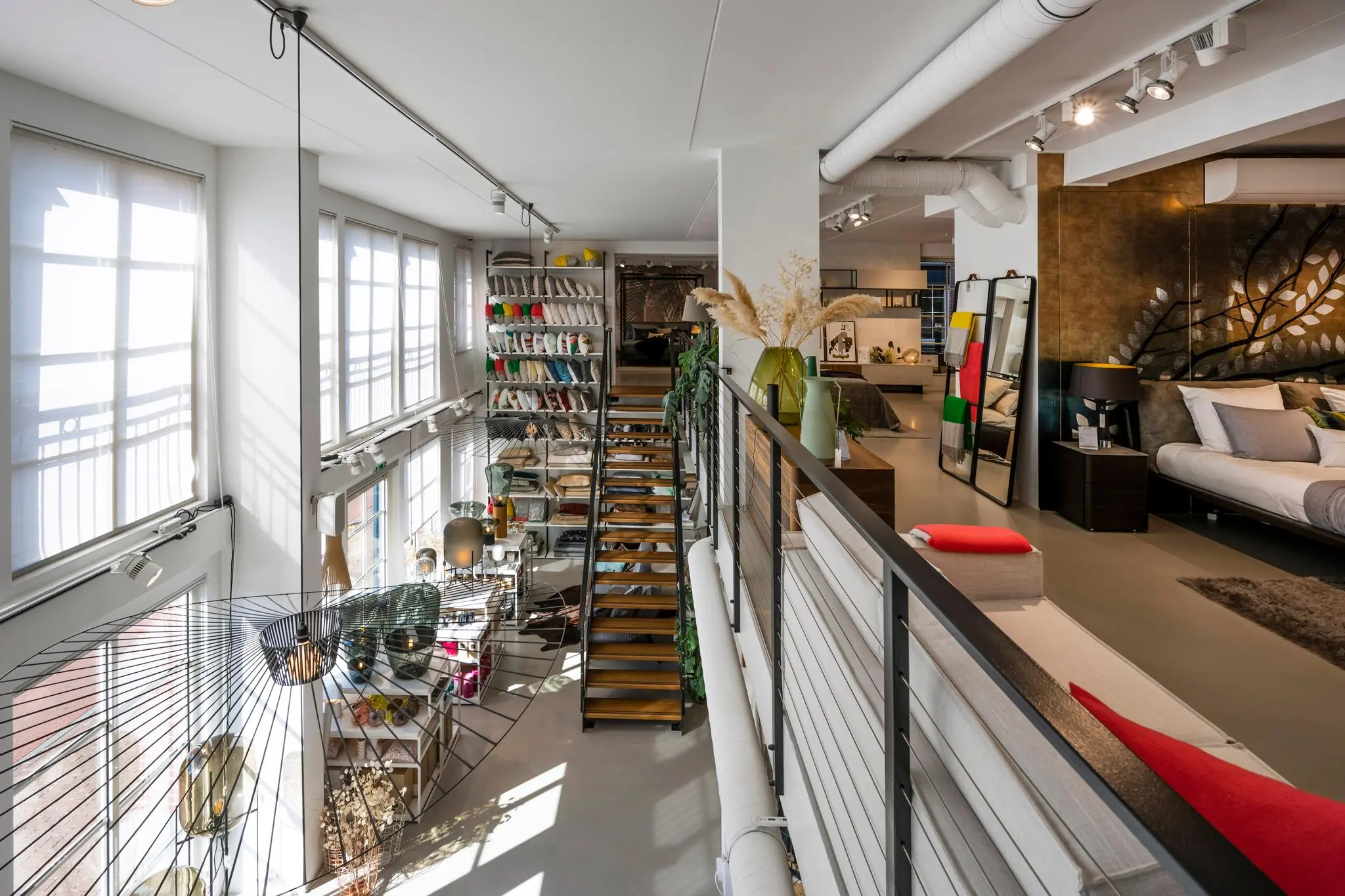 Modern interieur van een showroomwoning aan de Oostelijke Handelskade met een open trap, kleurrijke kussens en een stijlvol ingerichte slaap- en zitruimte.